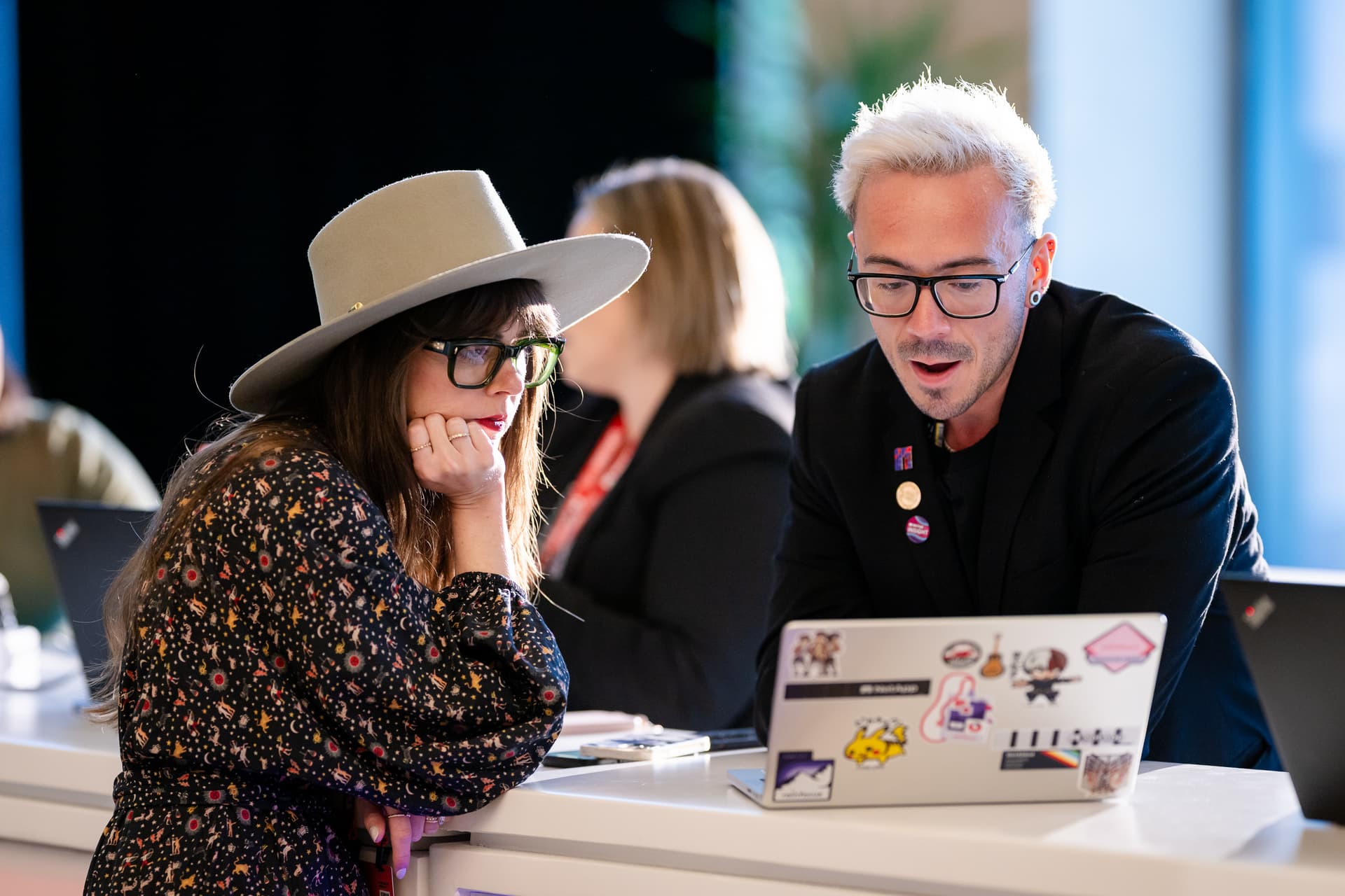 Two creative professionals collaborating over a laptop at an event booth