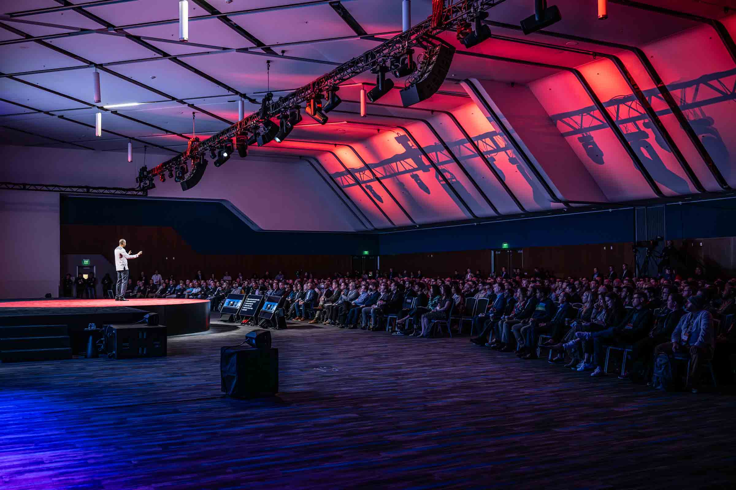 Speaker presenting on stage with dramatic red and blue lighting at corporate conference